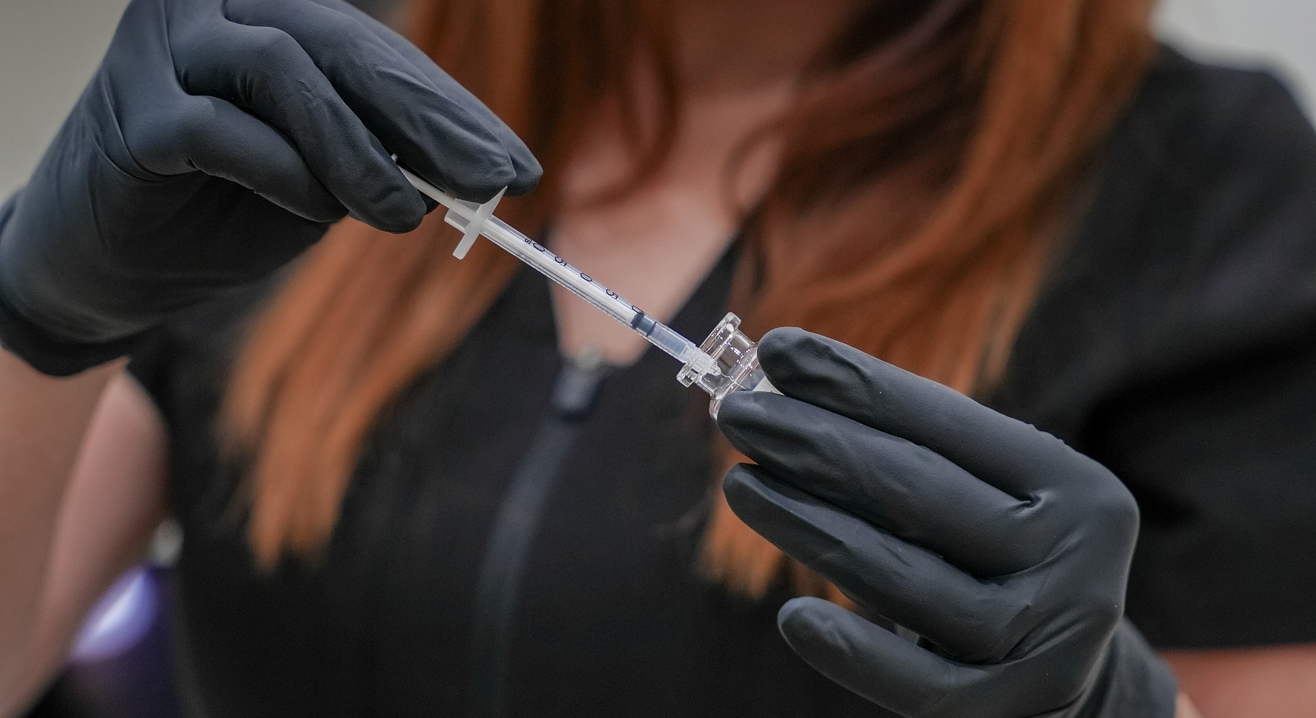 Hand holding syringe above a vial.
