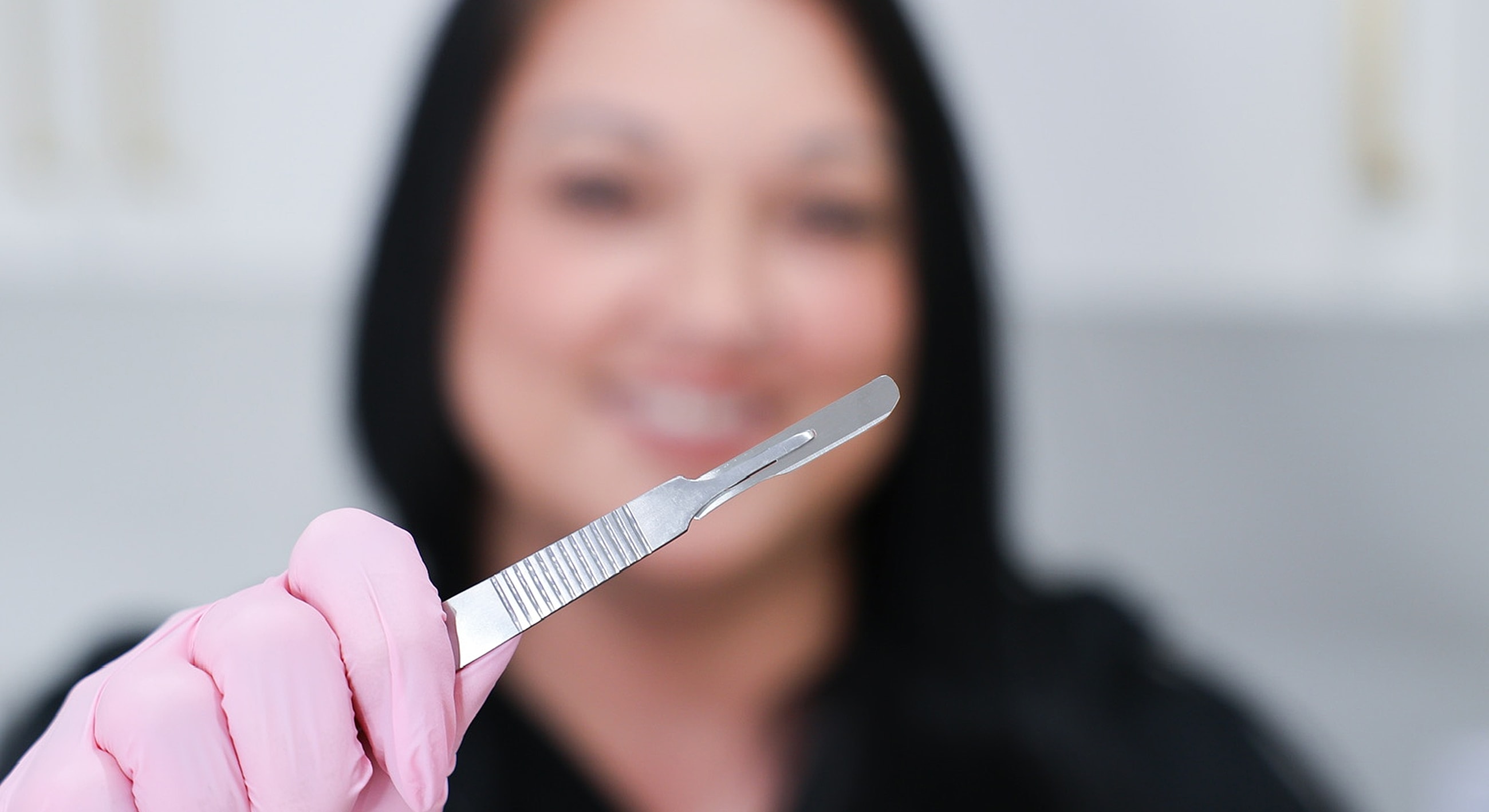 Professional holding a scalpel with pink gloves.